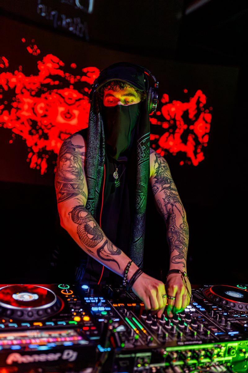 ryzl masked at the mixer in front of the red visuals